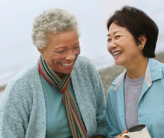 Two cheerful middle aged female friends talking on the beach