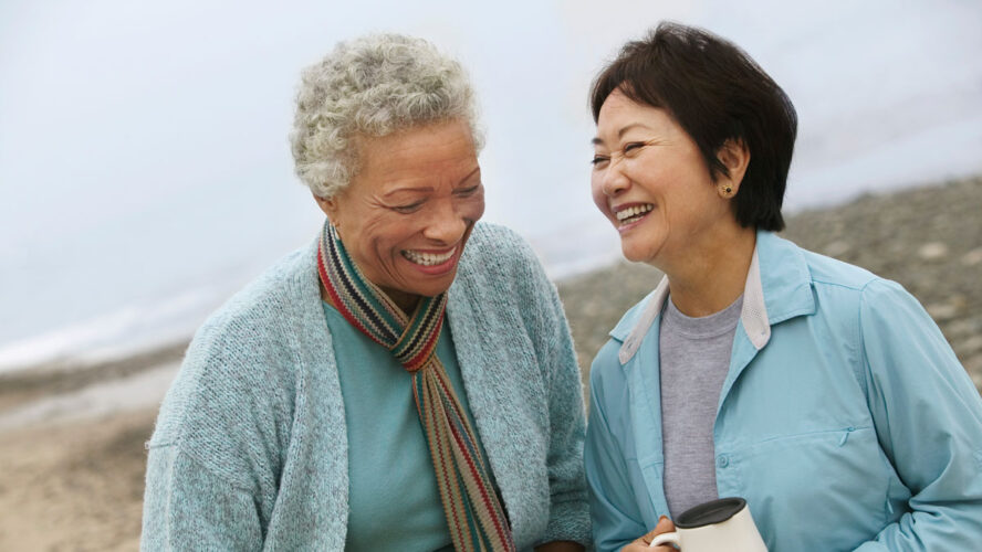 Two cheerful middle aged female friends talking on the beach
