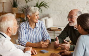 Group of four cheerful senior friends, two men and two women, sitting at table and enjoying talk after playing cards in assisted living home