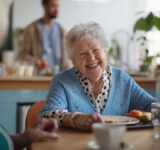 Smiling elderly woman enjoying breakfast in nursing home care center.