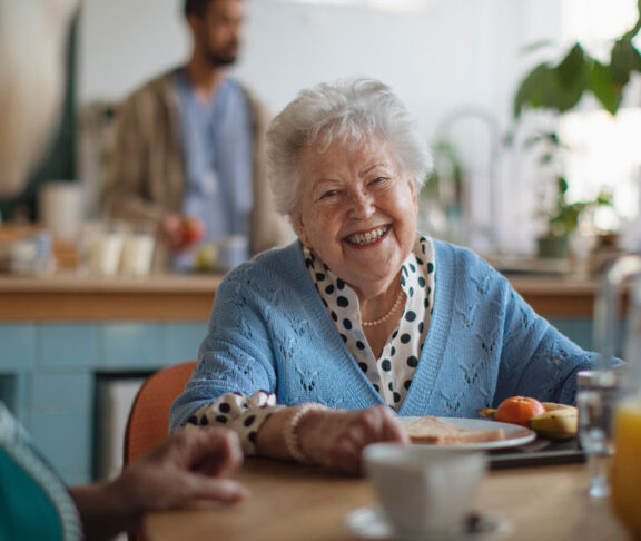 Smiling elderly woman enjoying breakfast in nursing home care center.