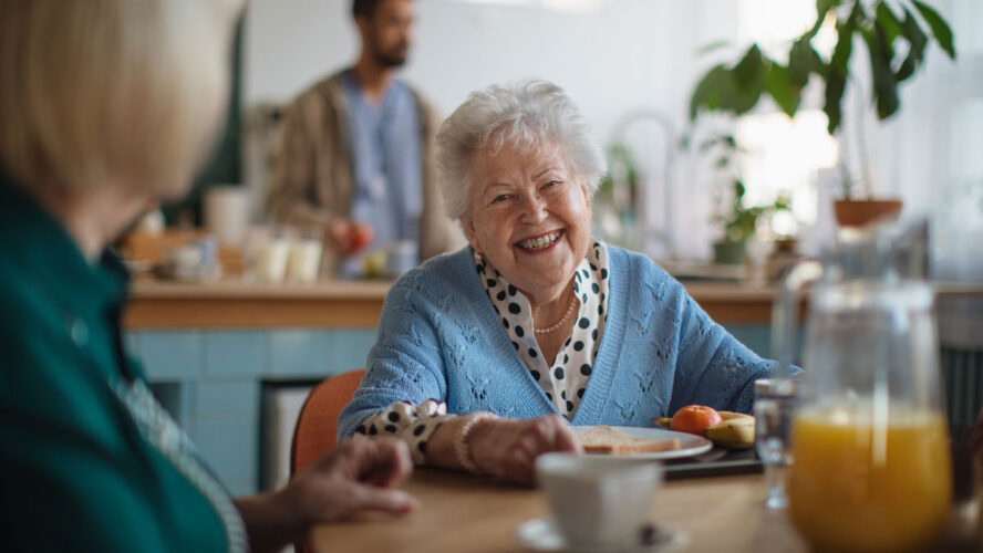Smiling elderly woman enjoying breakfast in nursing home care center.