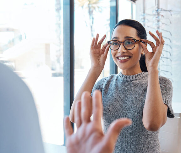 A customer buying, testing or trying on glasses at an optometrist store or shop. Health care eye wear professional picking or selling a pair of new eyeglasses to a young female client or patient