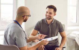 Portrait of a happy smiling young man patient in medical office listening to doctor holding report file with appointment and giving consultation during medical examination in clinic