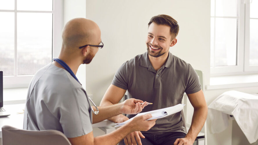 Portrait of a happy smiling young man patient in medical office listening to doctor holding report file with appointment and giving consultation during medical examination in clinic