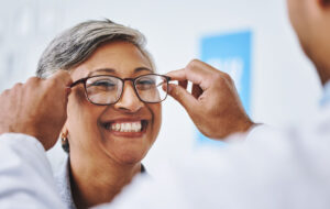 Optometry, smile and woman with prescription glasses, optician and helping client with product. Female person, employee and optometrist assist with eyewear, clear vision and buying new spectacles