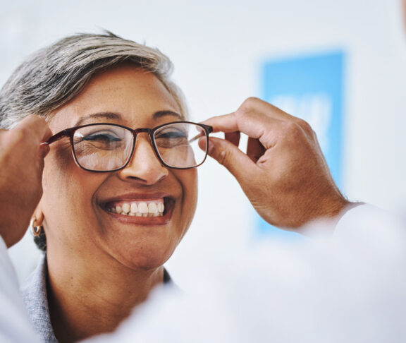 Optometry, smile and woman with prescription glasses, optician and helping client with product. Female person, employee and optometrist assist with eyewear, clear vision and buying new spectacles
