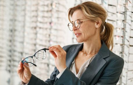 Woman in jacket chooses between two glasses in an optician's shop