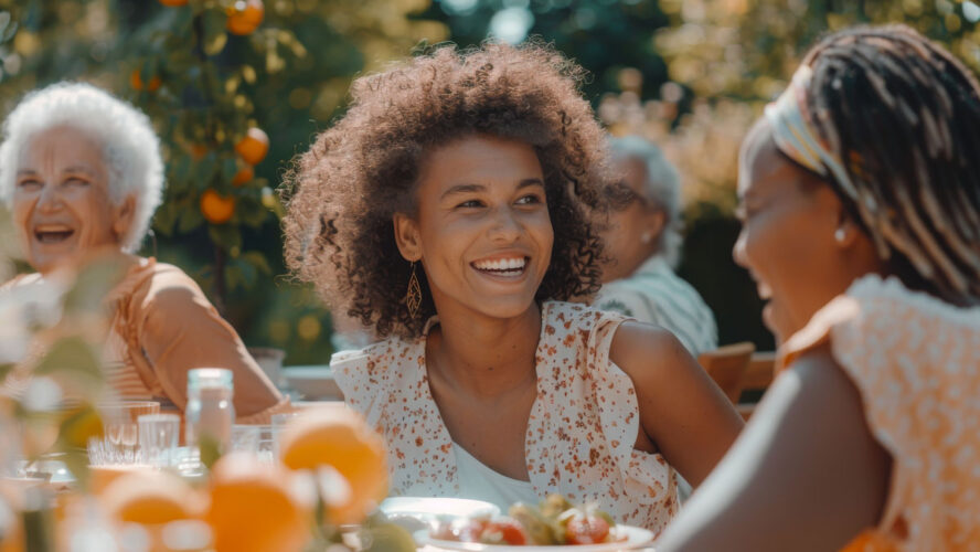 Laughing Multiethnic Female Talking with a Senior Woman at a Summer Garden Party. Children, Adults, and Older People Gathered at a Table to Enjoy Food and Have Fun