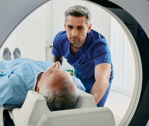 Senior man going into CT scanner. CT scan technologist overlooking patient in Computed Tomography scanner during preparation for procedure