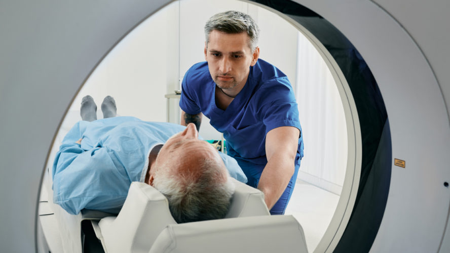 Senior man going into CT scanner. CT scan technologist overlooking patient in Computed Tomography scanner during preparation for procedure