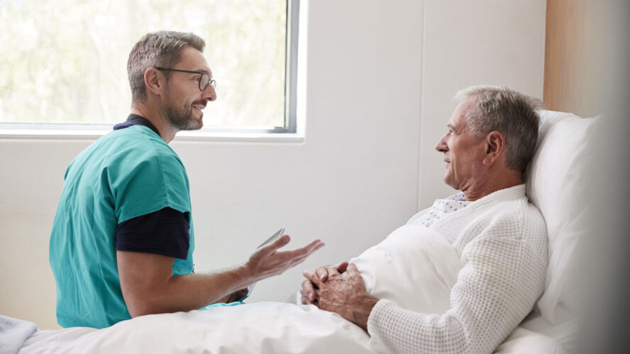 Surgeon Visiting And Talking With Senior Male Patient In Hospital Bed In Geriatric Unit