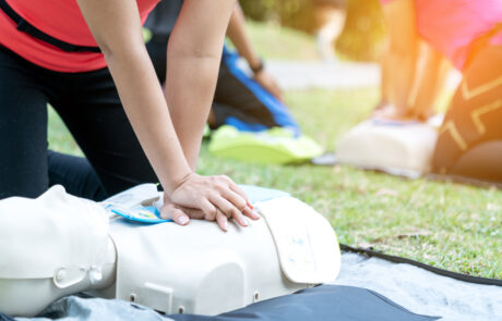 Asian female or runner woman training CPR demonstrating class in park by put hands and interlock finger over CPR doll give chest compression. First aid training for heart attack people or lifesaver.