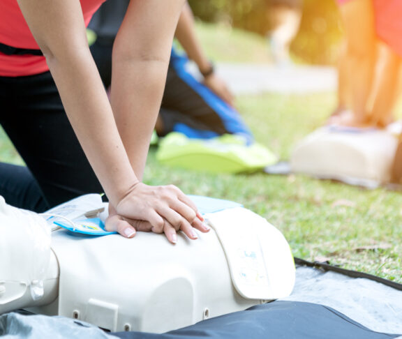 Asian female or runner woman training CPR demonstrating class in park by put hands and interlock finger over CPR doll give chest compression. First aid training for heart attack people or lifesaver.