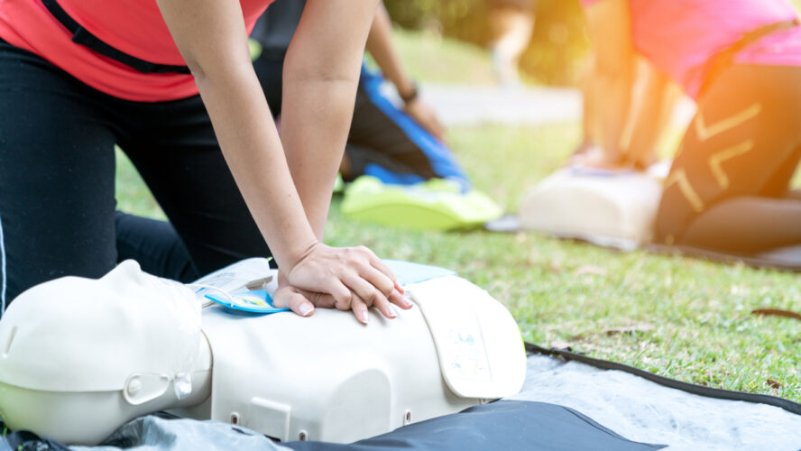 Asian female or runner woman training CPR demonstrating class in park by put hands and interlock finger over CPR doll give chest compression. First aid training for heart attack people or lifesaver.