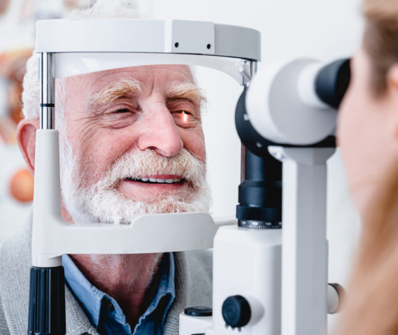 Smiling cheerful elderly patient being checked on eye by female ophthalmic doctor