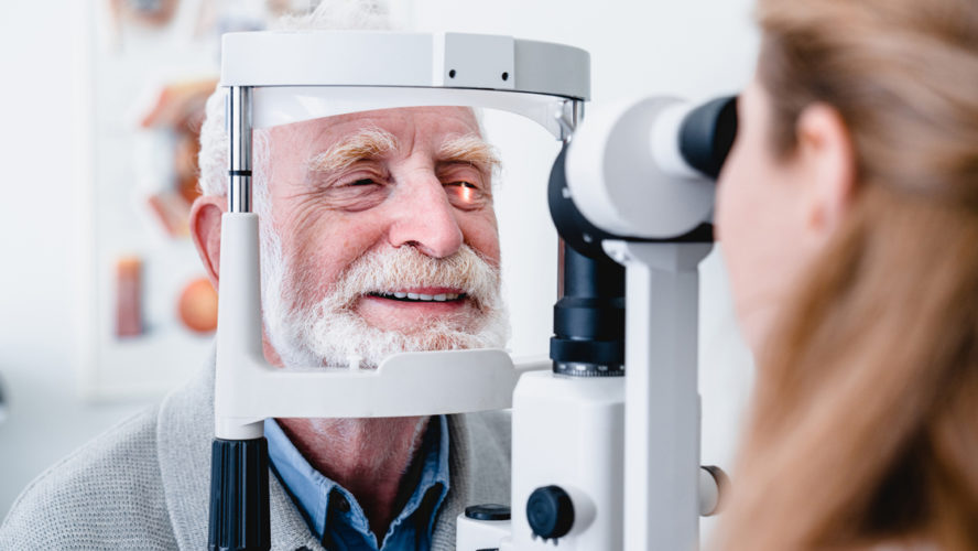 Smiling cheerful elderly patient being checked on eye by female ophthalmic doctor