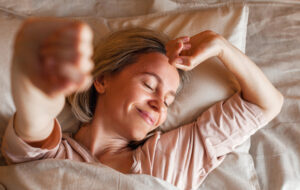 Good morning, new day, weekend, holiday. Happy middle aged woman lying on bed, lady stretching arms after sleep and enjoying morning in cozy comfort bedroom interior, free space