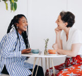 Two happy businesswomen chatting and laughing together during a coffee break in a cafe. Cheerful female business colleagues enjoying a friendly conversation in a coffee shop.