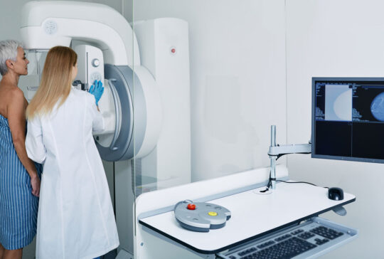 Mammogram procedure in medical clinic, mammography. Female mammologist positions mature woman at imaging machine to receive mammogram
