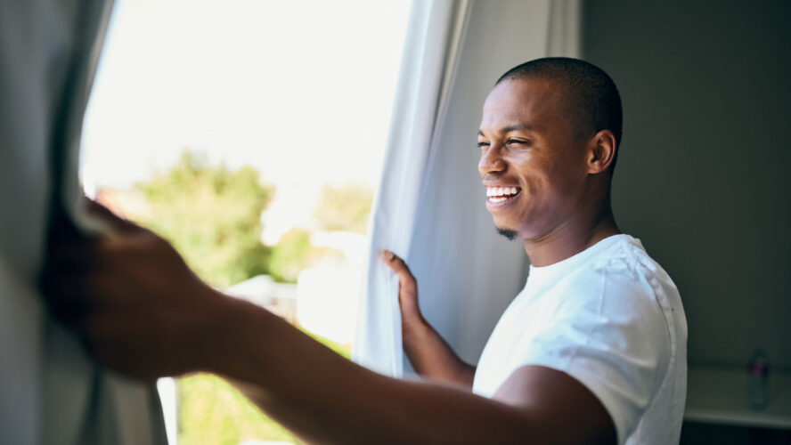 Shot a handsome young man opening his bedroom curtains in the morning
