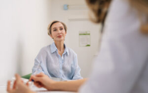 Closeup of unrecognizable female doctor in white uniform to middle-aged woman patient, discuss health concerns writes complaints, fill medical form. General checkup, healthcare concept