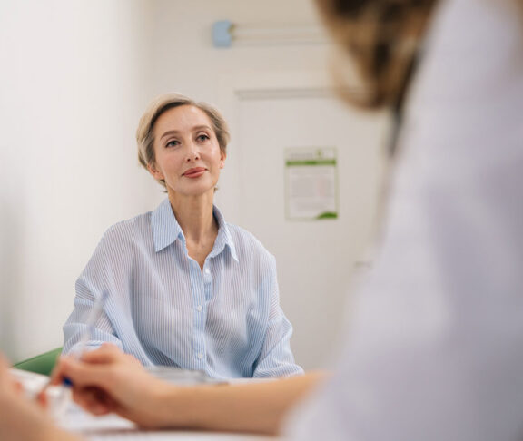 Closeup of unrecognizable female doctor in white uniform to middle-aged woman patient, discuss health concerns writes complaints, fill medical form. General checkup, healthcare concept