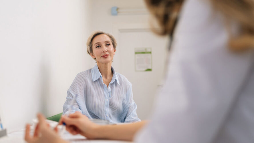 Closeup of unrecognizable female doctor in white uniform to middle-aged woman patient, discuss health concerns writes complaints, fill medical form. General checkup, healthcare concept