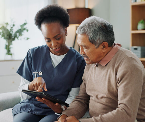Nurse, senior and discussion with tablet on sofa for healthcare, communication or consultation at home. Woman or medical caregiver helping and talking to elderly male person on technology for advice