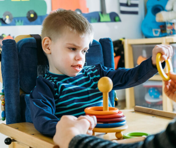 Activities for kids with disabilities. Preschool Activities for Children with Special Needs. Boy with with Cerebral Palsy in special chair play with mom at home