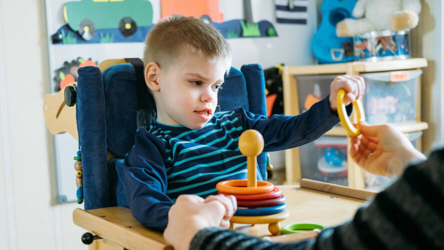 Activities for kids with disabilities. Preschool Activities for Children with Special Needs. Boy with with Cerebral Palsy in special chair play with mom at home