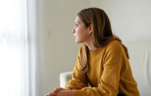 Melancholic sad woman looking through the window at home