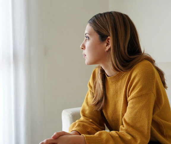 Melancholic sad woman looking through the window at home