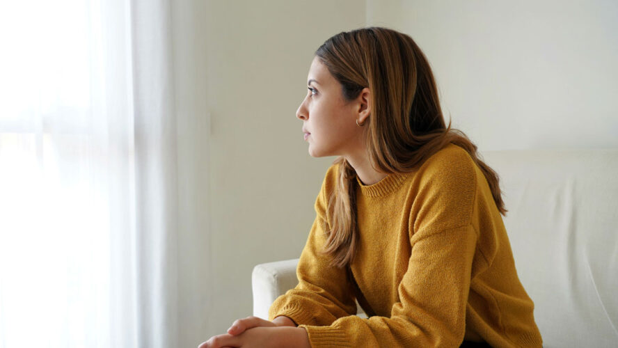 Melancholic sad woman looking through the window at home