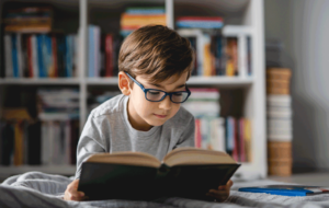 One caucasian boy lying on the floor at home in day reading a book front view wearing eyeglasses copy space real people