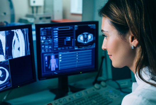 Radiologist reading a CT scan. Female doctor running CT scan from control room at hospital