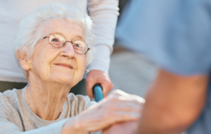 Holding hands, caregiver and senior woman in wheelchair for support outdoor in retirement home. Love, trust and healthcare nurse or medical wellness doctor for disability patient with kindness